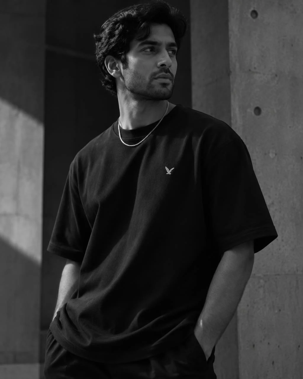 Man wearing a black unisex tee with a small silver bird graphic and a silver necklace