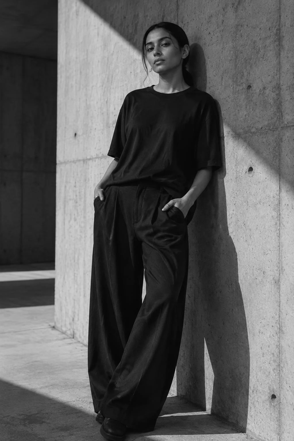Woman in an oversized black tee and flowing trousers against a concrete wall